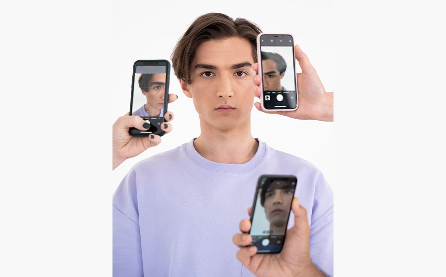 Young man surrounded by smartphones taking his photo from different angles, symbolizing social media pressure and beauty standards.