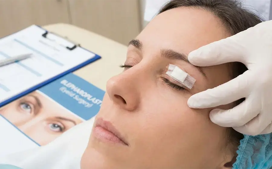 Patient applying cold compress after eyelid surgery to reduce swelling and bruising during blepharoplasty recovery