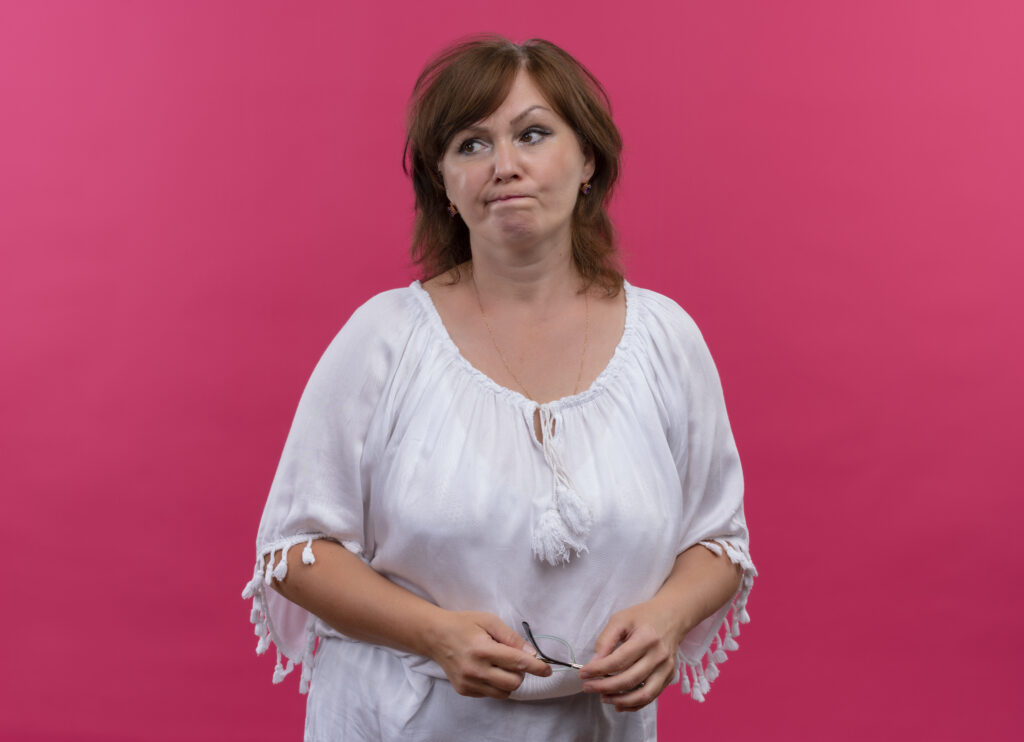 confused middle aged woman holding glasses isolated pink wall