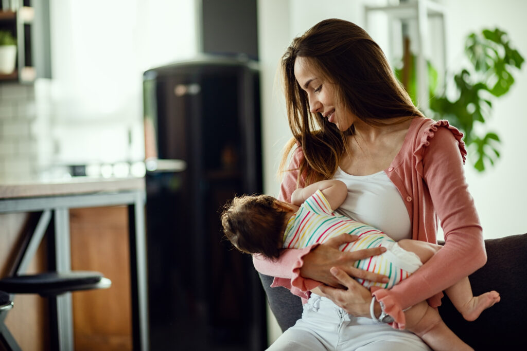 smiling mother breastfeeding her baby daughter while being home