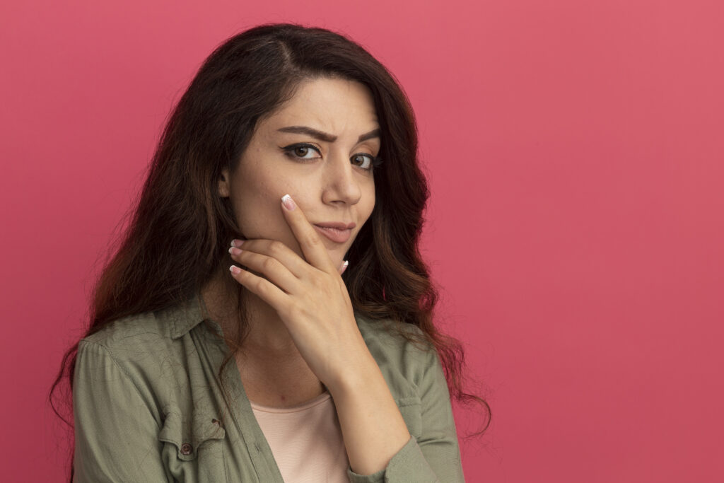 thinking young beautiful girl wearing olive green t shirt grabbed chin isolated pink wall with copy space