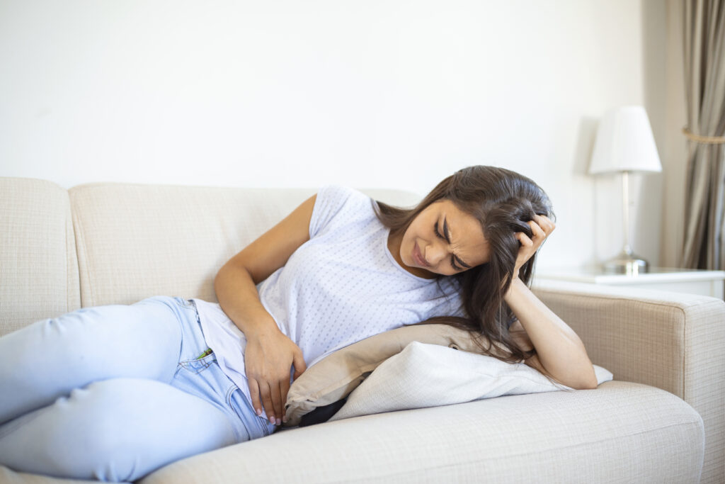 woman painful expression holding hands against belly suffering menstrual period painsitting sad home bed having tummy cramp female health concept