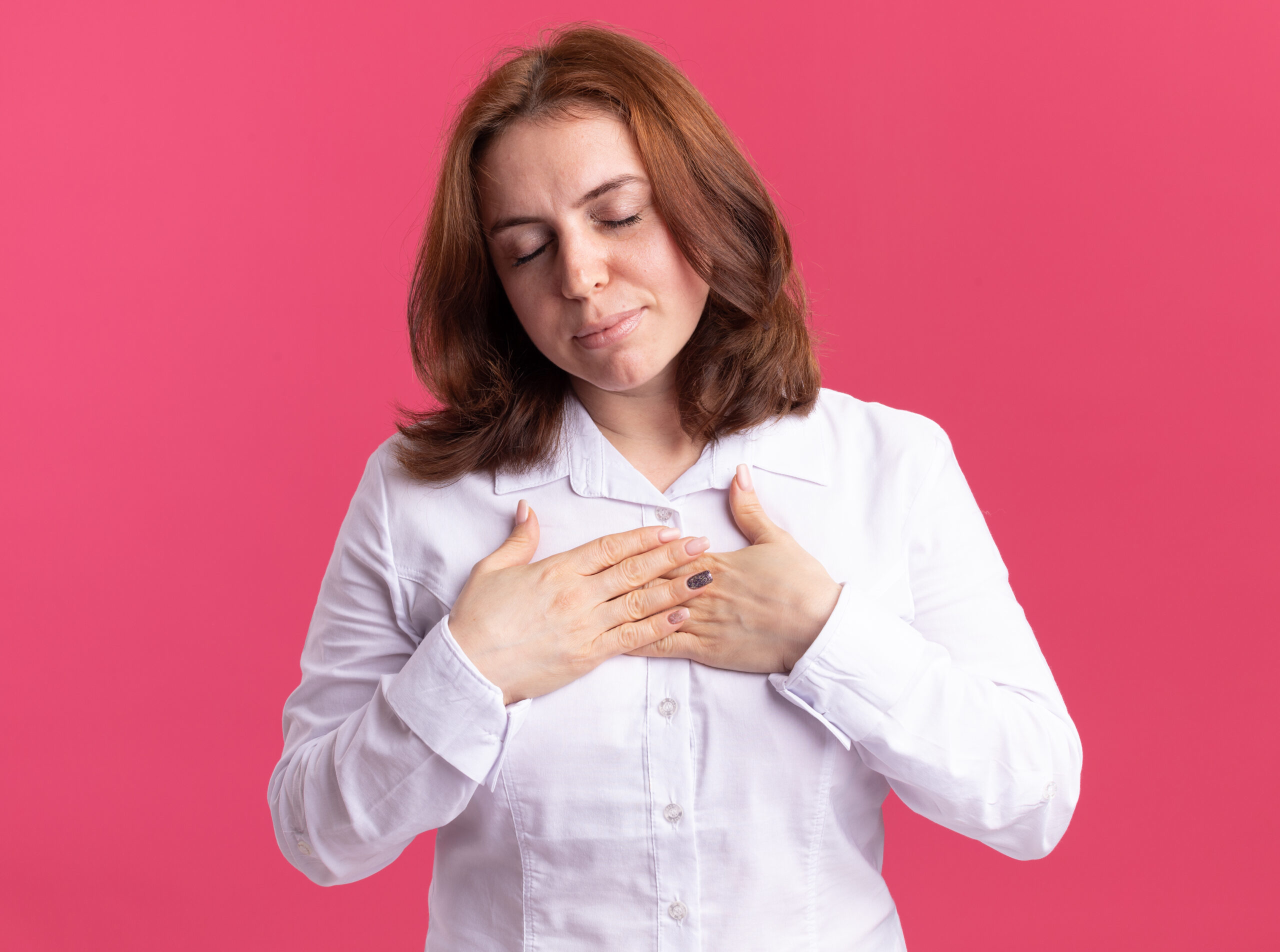 young woman white shirt holding hands her chest feeling thankful standing pink wall scaled