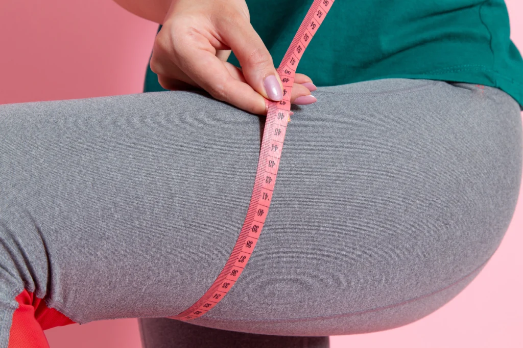 front view young female green t shirt measuring her sizes pink wall waist sport exercise workout beauty slim athlete.jpg