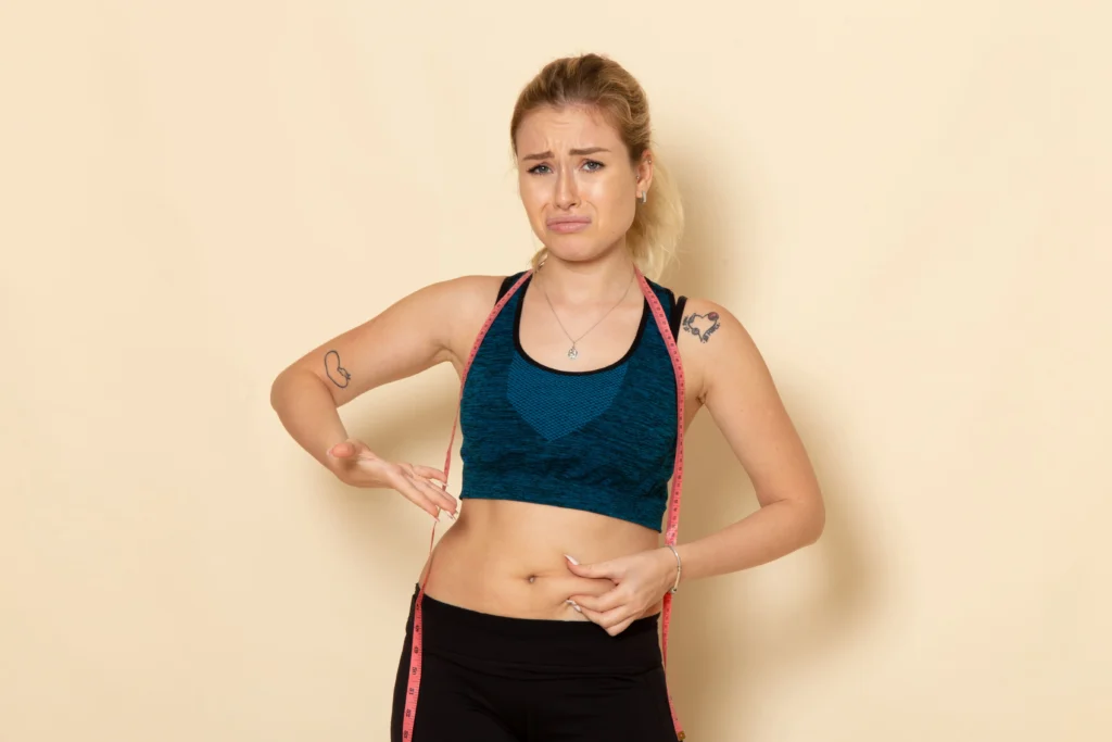 front view young female sport outfit measuring her body sad due her weight.jpg